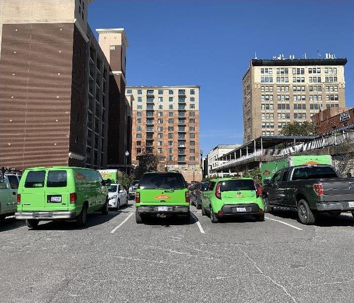 Multiple SERVPRO vehicles parked in parking lot with several commercial building in background.
