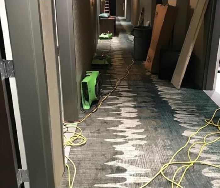 Water damage in commercial building hallway; SERVPRO restoration equipment being used
